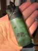 Hand holding a green jade necklace with intricate carvings on a blurred background