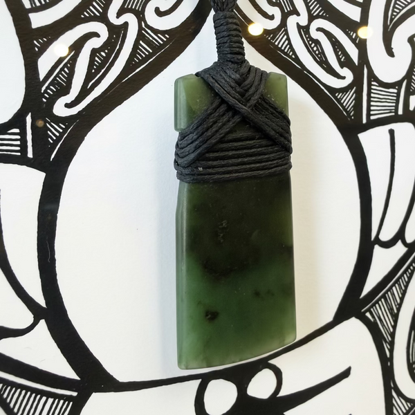 Green stone pendant with black cord on a decorative background