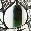 Green stone pendant with black cord on a decorative background