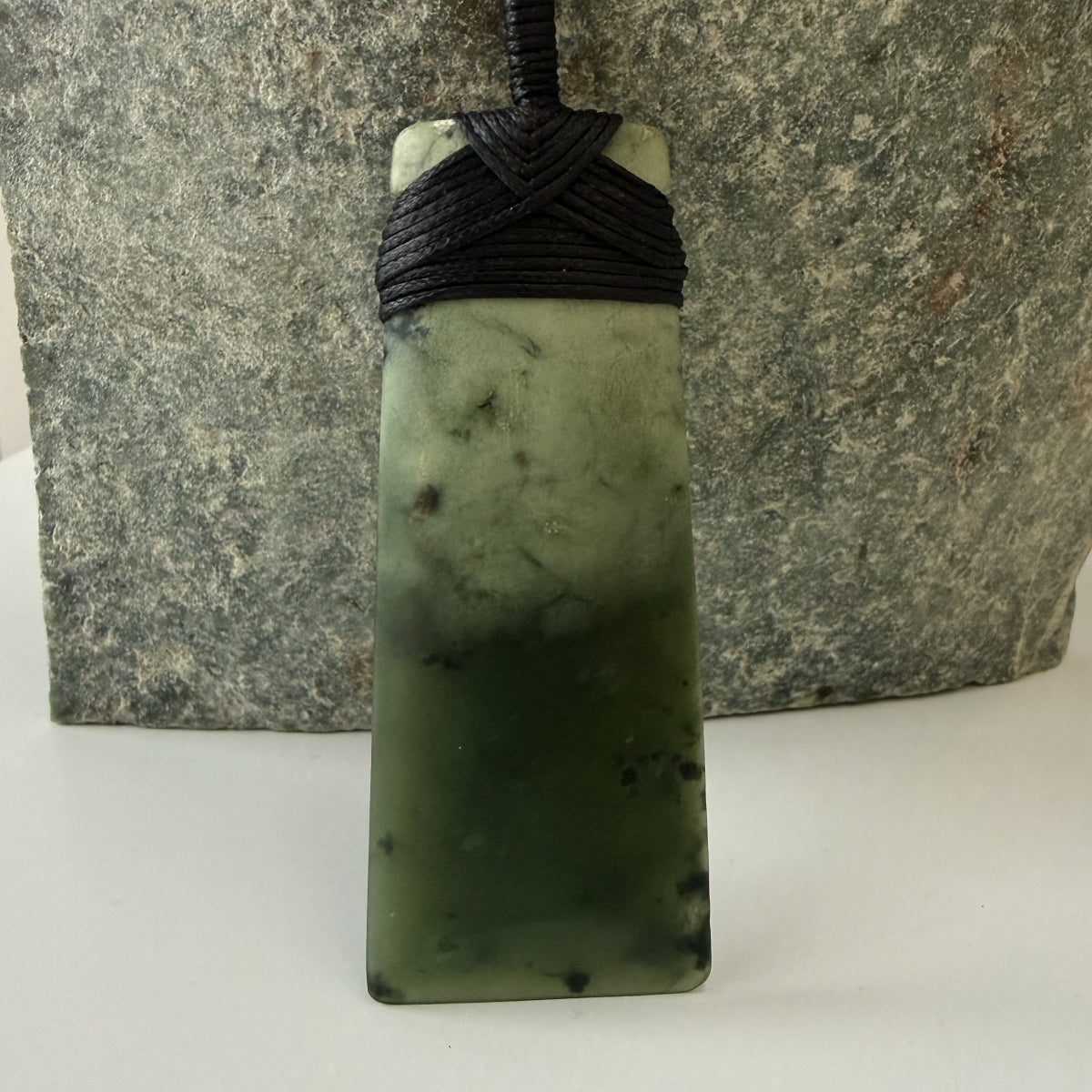 Green stone pendant with black cord against a stone background