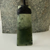 Green stone pendant with black cord against a stone background