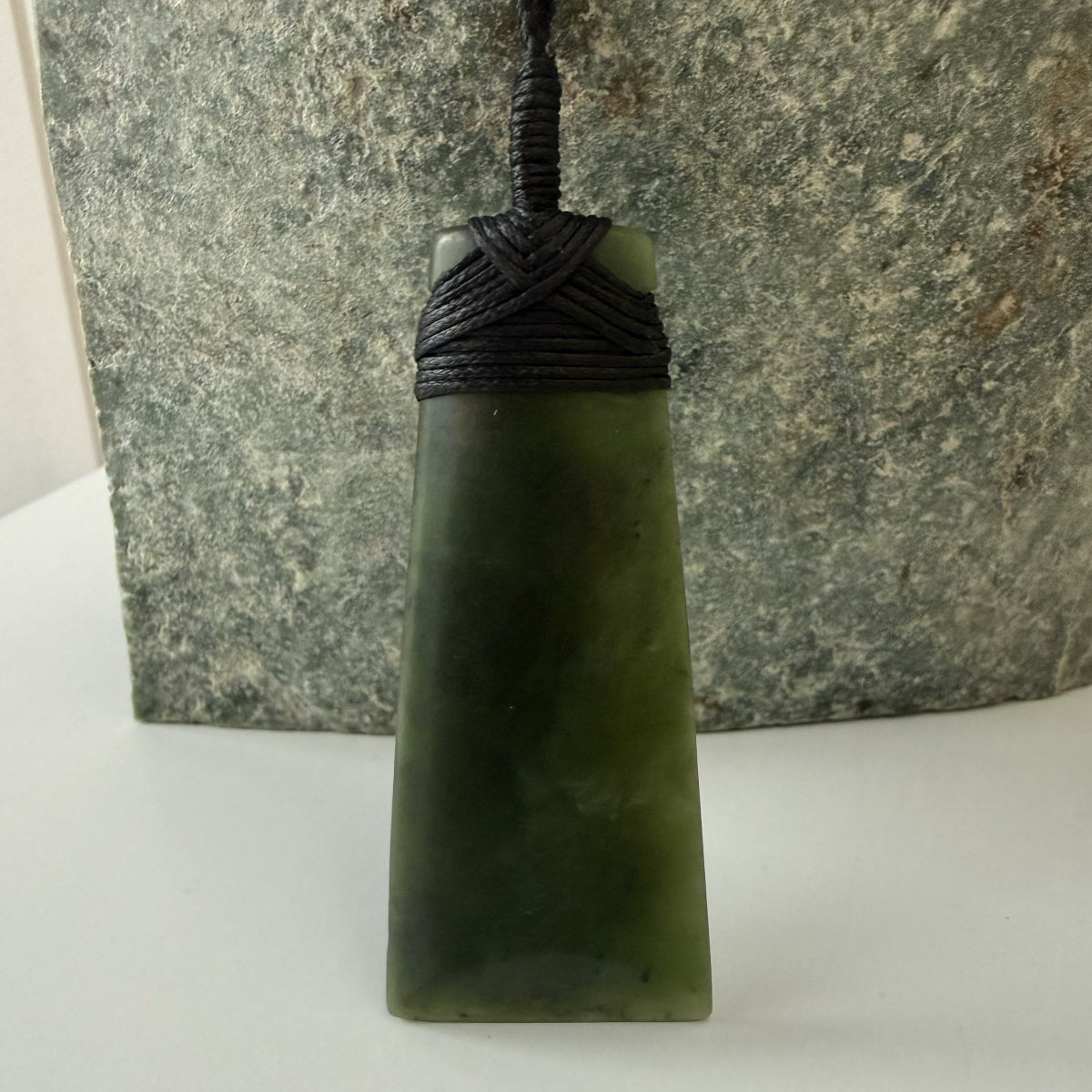 Green jade pendant on a black cord against a stone background