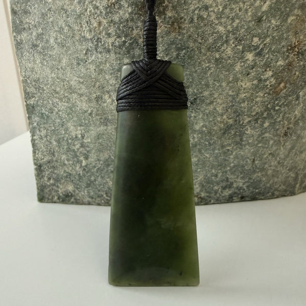 Green jade pendant on a black cord against a stone background