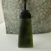 Green jade pendant on a black cord against a stone background