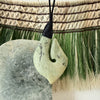 pounamu greenstone hook pendant on a string against a woven Harakeke Maori Korowai